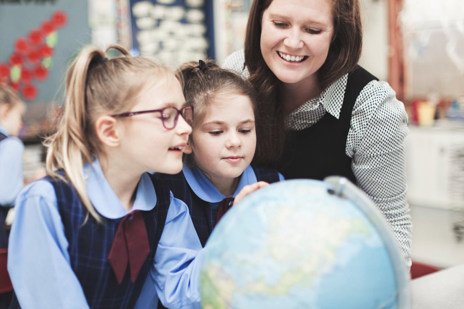 Smiling female teacher looking at globe with young students