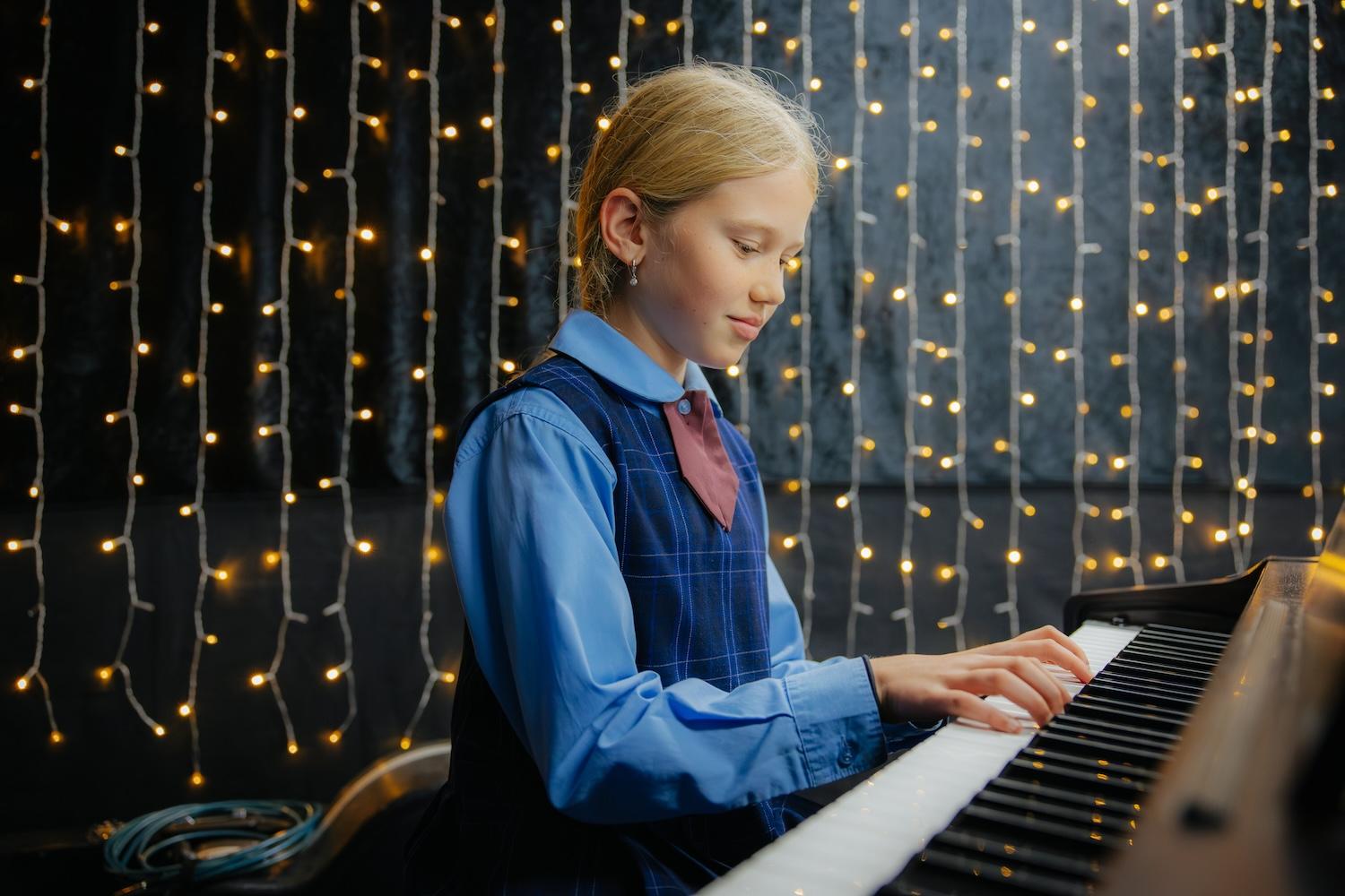 Female student with blonde hair playing piano with fairy lights hanging behind her