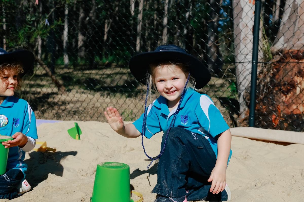 Young prep student smiling, waving, and playing in the sandpit at Port Stephens school.