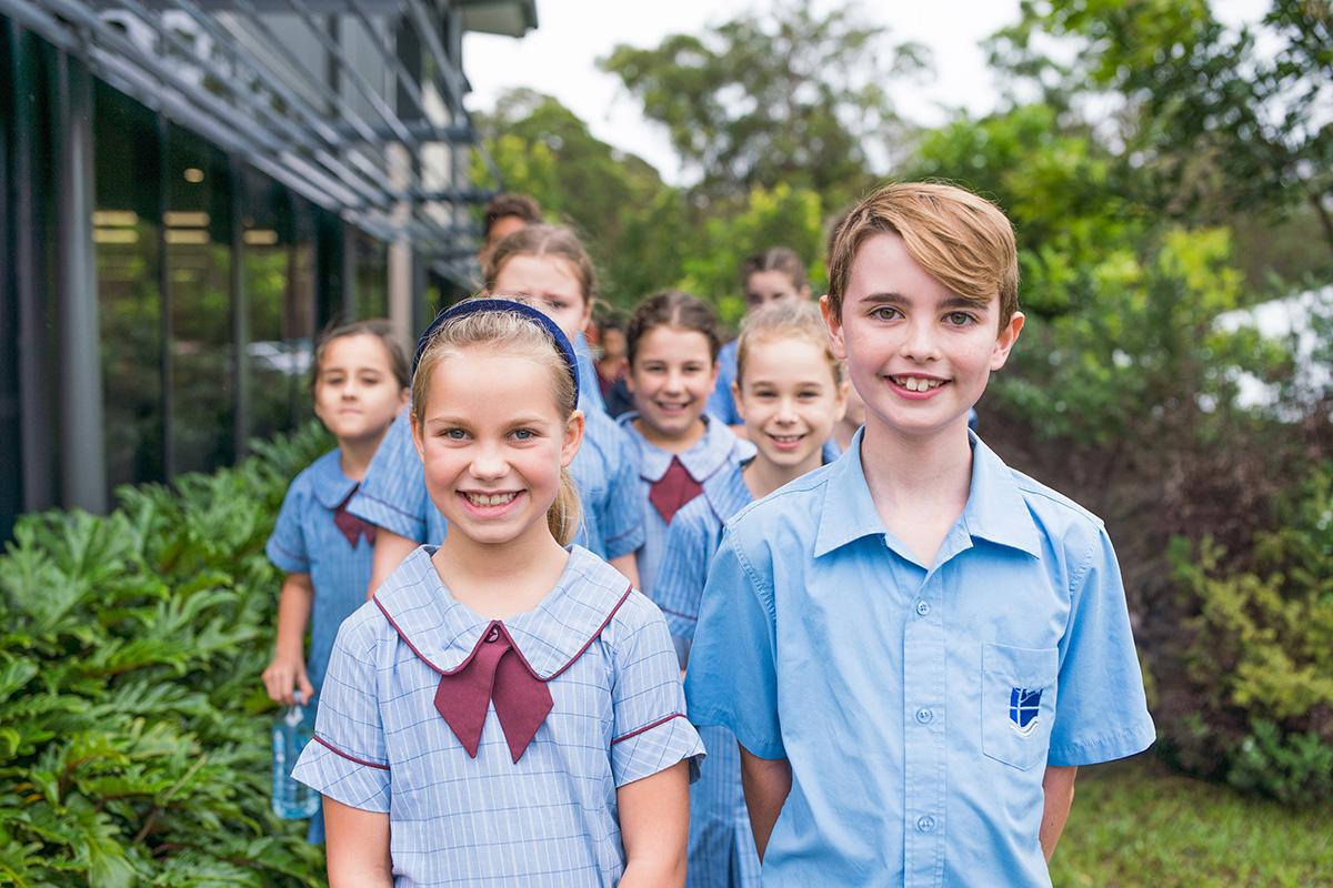 Primary school students smiling and welcoming arrivals during a school tour outdoors.