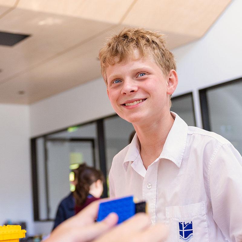 A student at Medowie Christian School smiling during a classroom activity, highlighting the welcoming community.