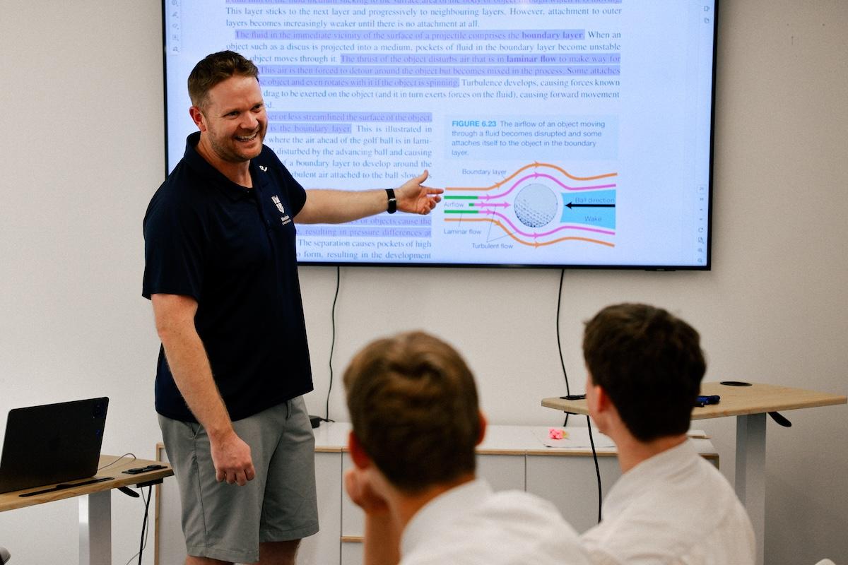 Male science teacher leading a classroom lesson explicit direct instruction, using a scientific diagram.